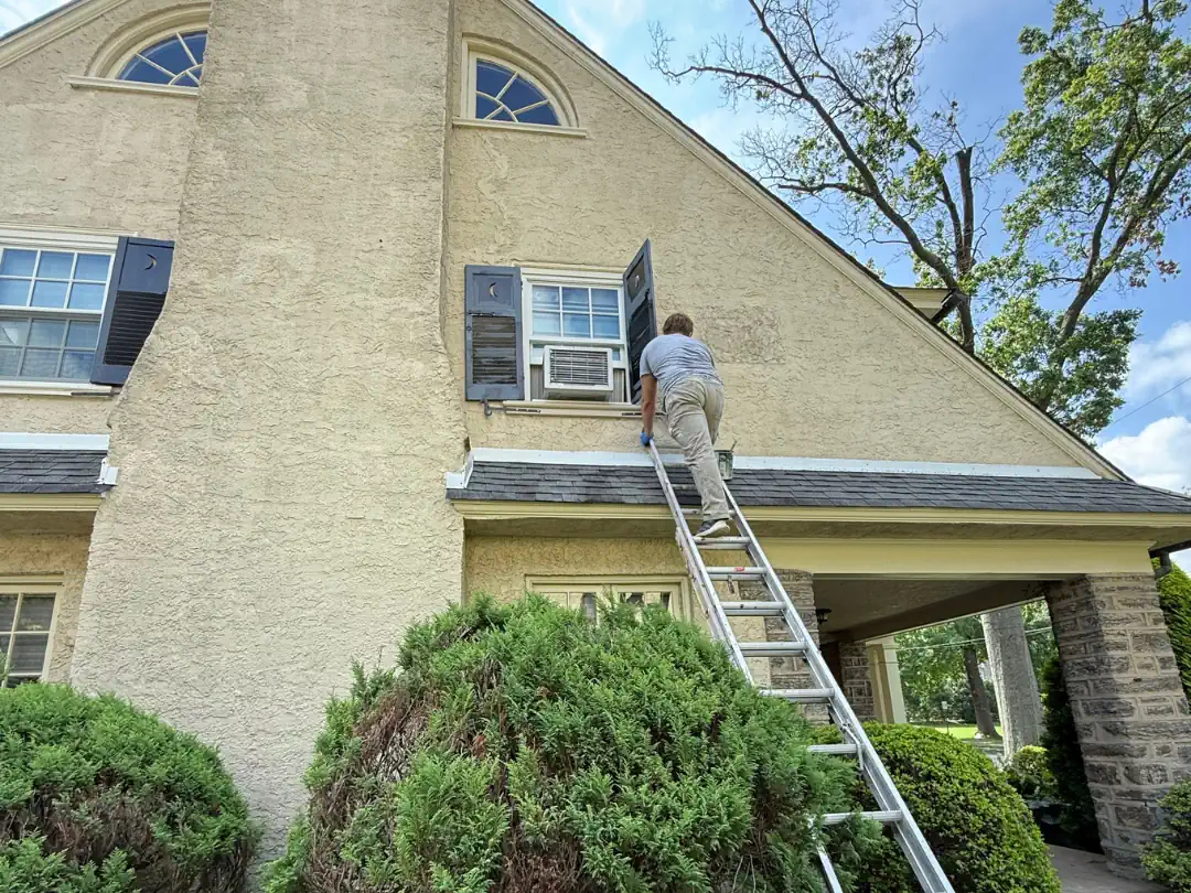 Painter on ladder prepping and painting stucco exterior on a two-story home — SIB PRO PAINTERS, Bucks County, PA